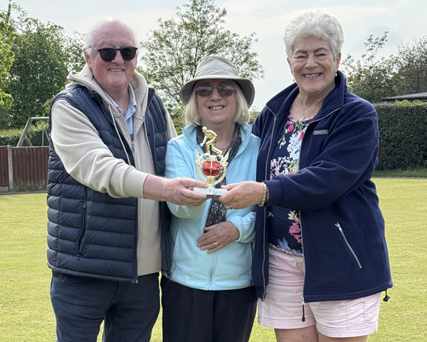 Two women and a man standing on the green, holding a small trophy.