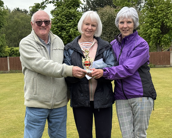 A man and two women standing on the green, holding the small trophy.