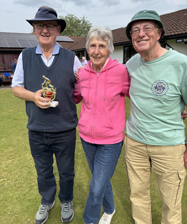 Woman standing between two men. The man on the left is holding the small trophy.