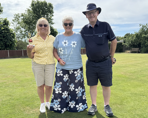Two women and a man standing on the green. The woman on the left is holding a small trophy.