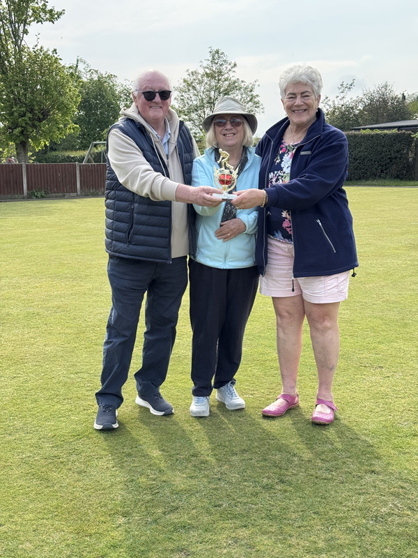 Two women and a man standing on the green, holding a small trophy.