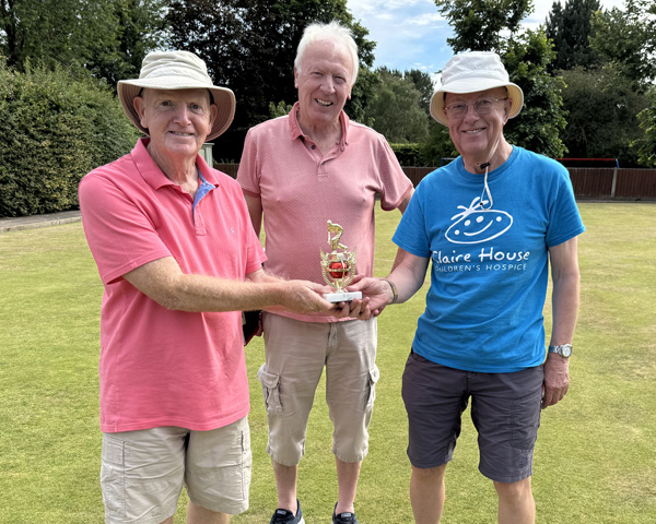 Three men standing on the green. The men on the left and right hand sides are holding the trophy between them.