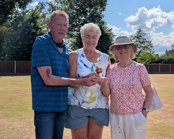 A man and two women standing on the green holding the small trophy