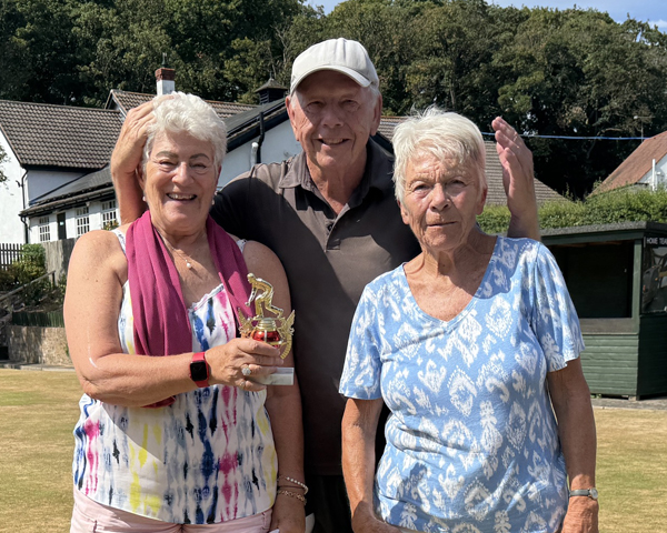 Two women and one man on the green. The woman on the left is holding the small trophy.