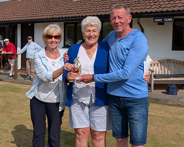 Two women and a man on the green, holding the small trophy
