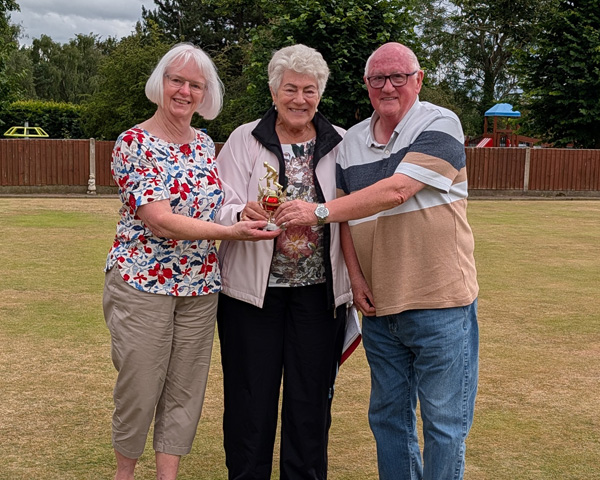 Two women and a man standing on the green, holding the small trophy.