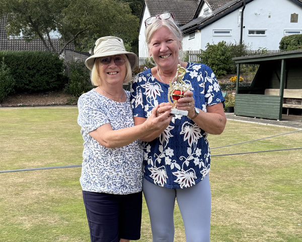 Two women standing on the green, holding the small trophy