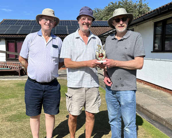 Three men standing on the green. The two men on the right are holding the small trophy.