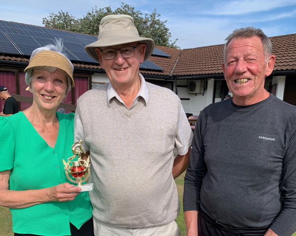 Two men and woman standing on the green. The woman is holding the small trophy.