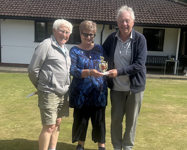 Two men and a woman standing on the green. The woman and the man on the right are holding the small trophy.