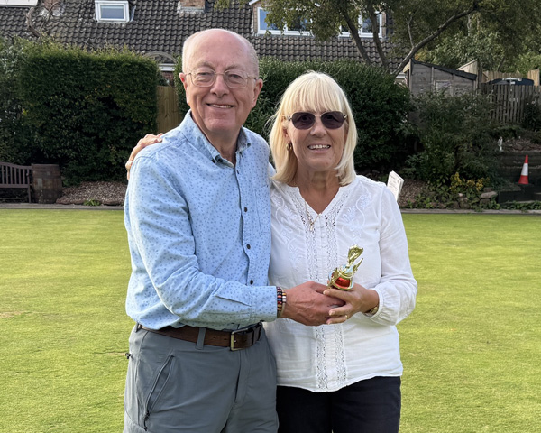 Man and woman standing on the green, holding the small trophy.