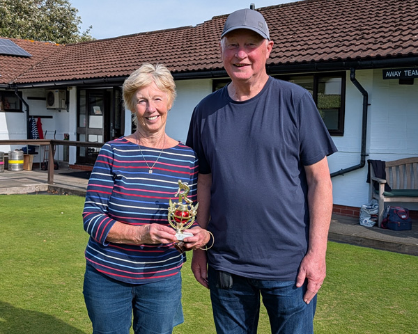 Woman and man on the green. The woman is holding the small trophy,